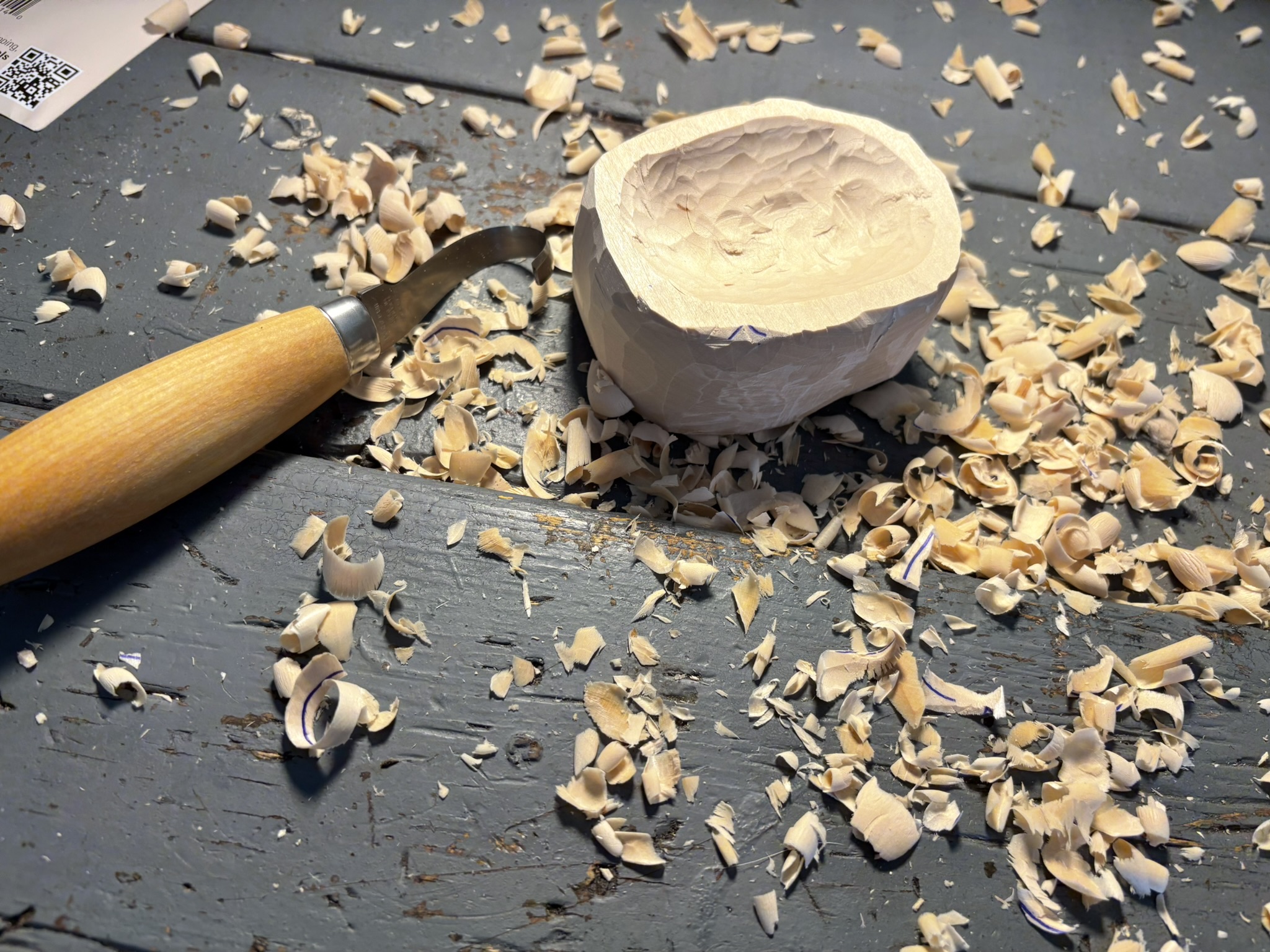 Carving shavings surround the rough basswood bowl on a workbench.