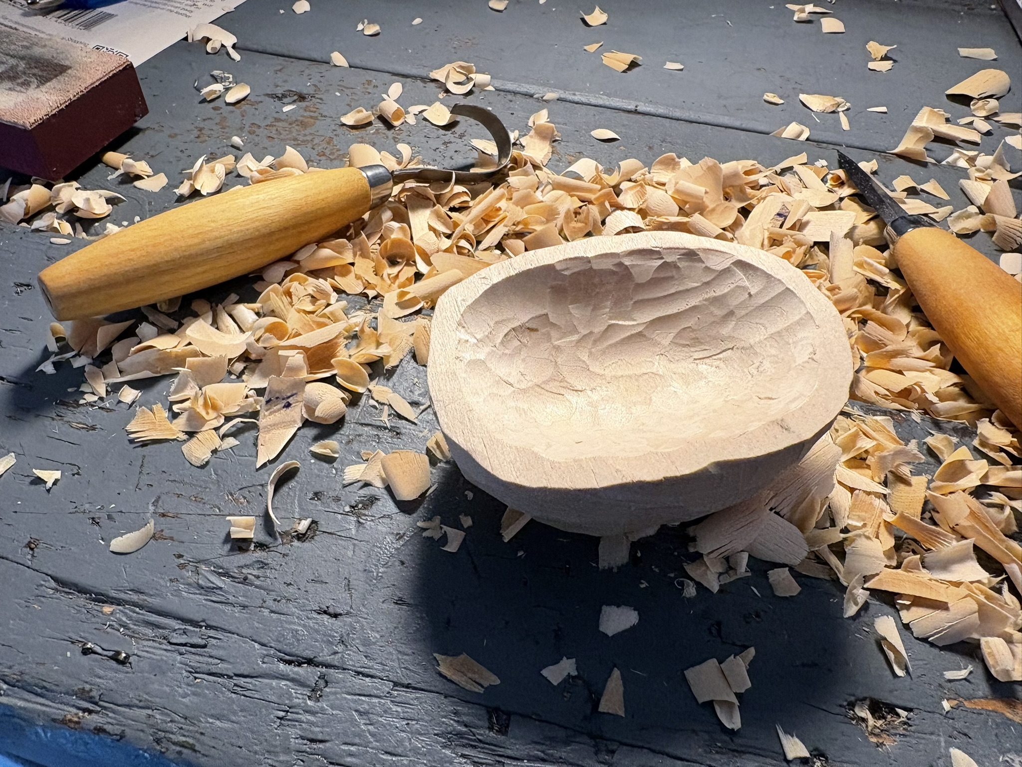 The partially carved bowl on a workbench with the straight and hook carving knives.